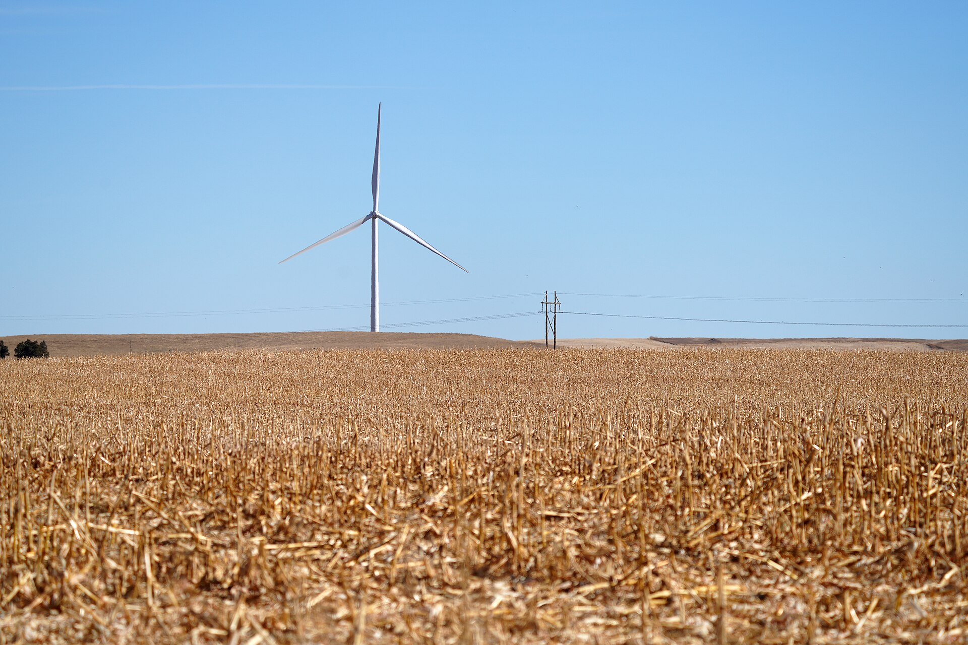 A single wind turbine standing beyond a harvested field under a clear sky.